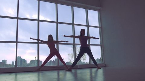 Two lovely yoga women doing yoga together in studio with large windows