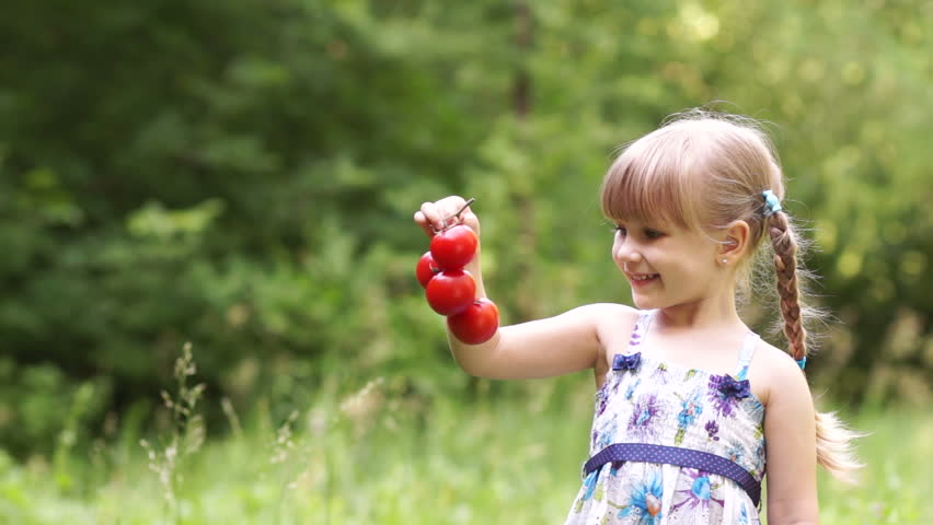 Child holding a tomato and looking at camera
