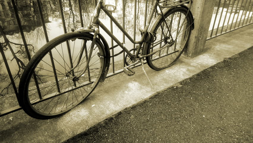Retro bicycle standing near river tied to fence, vintage old fashioned vehicle