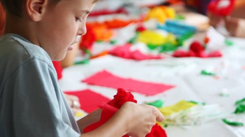 boy together with other children makes flower of color paper