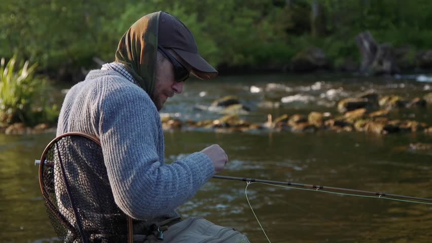 A fly fisherman changing fly by the river