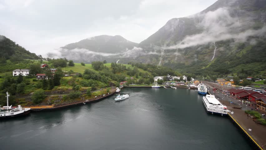 port in fiord valley with houses and floating ship in middle of foggy mountains
