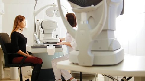 Modern ophthalmologist examining attractive woman's eyes with modern equipment, slider