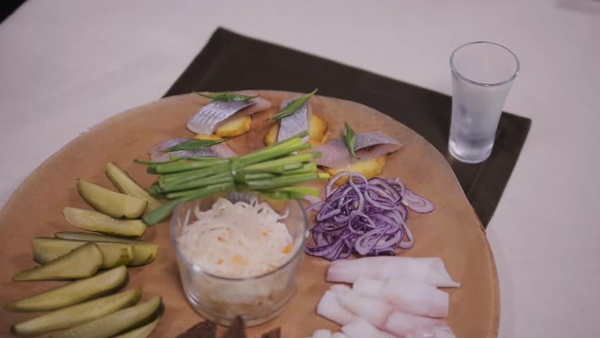 Traditional russian snacks salted herring with vegetables, onion, lemon, yellow lime, bread and shots of pouring vodka.