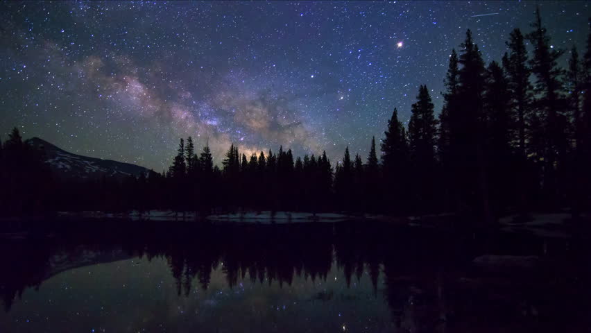 Astrophotography time lapse with tilt down motion of milky way galaxy over reflective alpine lake in Yosemite National Park, California