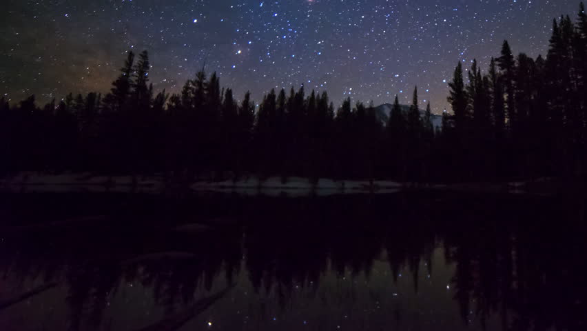 Astrophotography time lapse with zoom out motion of milky way galaxy rising over alpine lake reflection in Yosemite National Park, California