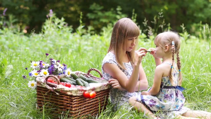 Mother and daughter with vegetables in nature. They eating cucumbers
