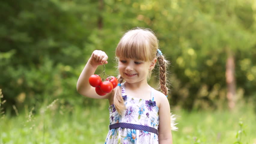 Child holding a tomato. Touching the vegetable and looks into the camera
