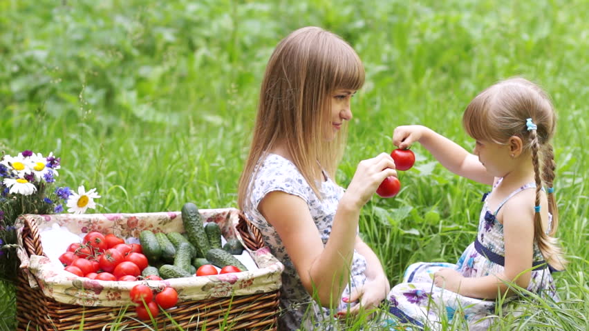 Mother and daughter with vegetables outdoors. They hold tomatoes and looking at