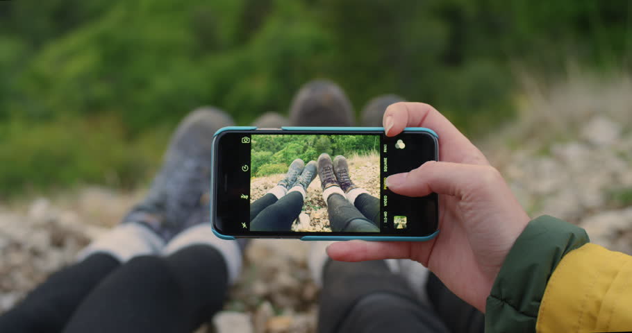 Two backpacker girl friends taking photograph of feet with smart phone women enjoying vacation travel adventure
