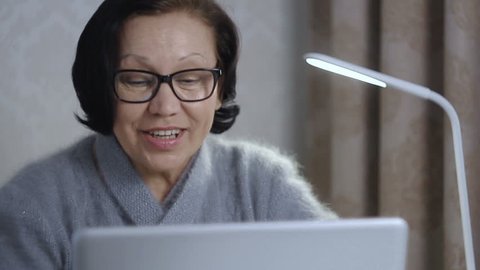 Elderly woman in black glasses speaks at computer