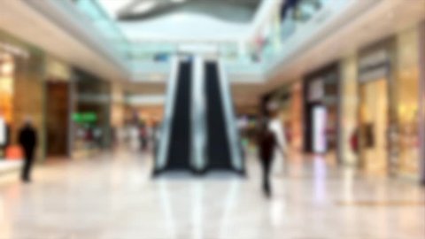Shopping mall retail shops escalator people pedestrian consumer purchase spending blurred abstract background