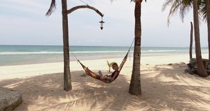 Video of attractive female freelancer making remote job via laptop computer and 4G internet while relaxing on tropical resort in hammock inspiring by ocean scenery shooting can be used on advertising