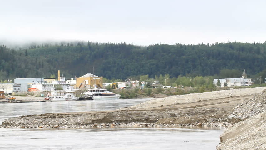 Dawson City, Yukon Canada on the Yukon River. Pan across fast flowing river of downtown Dawson. Ferry boat ready to load vehicles. Center of the old Klondike gold rush.