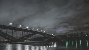 Time Lapse Tilt of arch bridge and river at night. Fast moving clouds and ice in the water