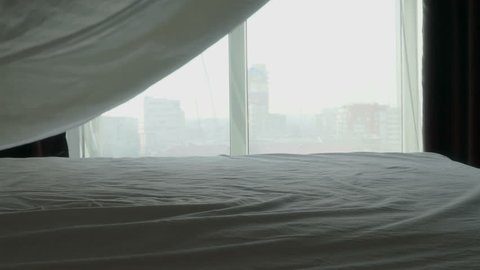 Making bed in high rise apartment bedroom in the morning. Blanket flying in slow motion.