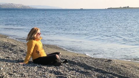 Relaxed middle aged woman  warmly clothed in a cold winter on the beach sitting alone