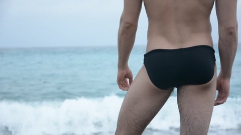 Back view of sexy unrecognizable man in trunks on beach against of sea