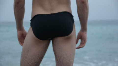 Back view of sexy unrecognizable man in trunks on beach against of sea