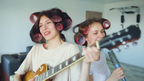 Two funny girls singing with comb and playing electric guitar, dancing, singing,  and having fun at home.