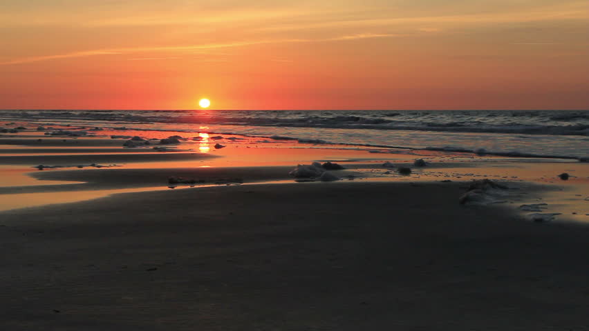 Foamy beach sunrise.  Sea foam is washing up on the beach in this low angle shot of the colorful sunrise just rising above the horizon