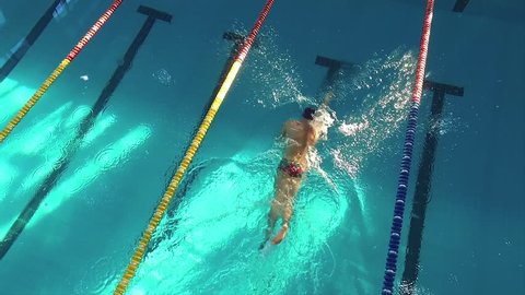 Flight over male swimmer swims in a pool HD aerial video. Front crawl freestyle. Professional athlete training on water lane