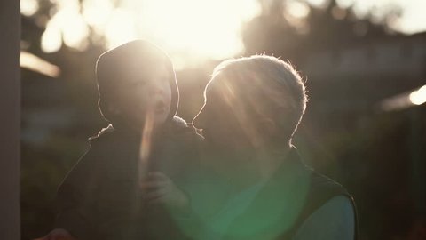 CLose-up of grandfather holding grandson on hands, hugs and kiss boy on cheek. Old man standing outdoor in sunlight. 4K