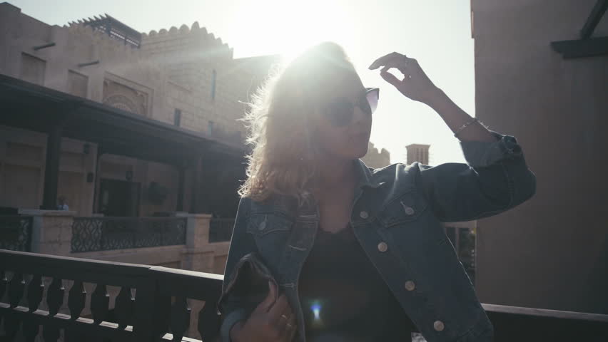 UAE, 2017: Madinat jumeirah. Beautiful young woman in sunglasses standing on the background of the sun and straightens hair. Stylish girl stands on the background of the historical sights of Abu Dhabi