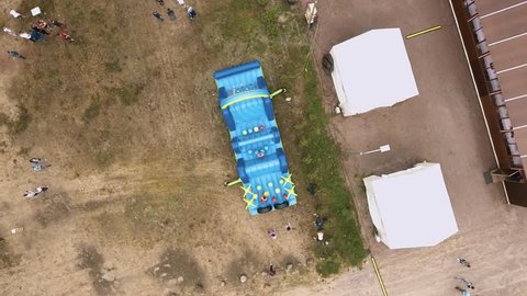 SAINT PETERSBURG, RUSSIA - JULY 30, 2016: Aerial top shot topless man jumping on blue inflatable obstacle course on sand in summertime