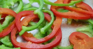 Close video of cutting sliced green and red bell peppers in a stainless steel skillet with a black nylon spatula.