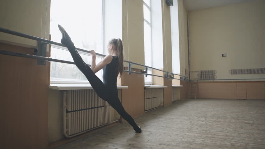 Young graceful female ballet dancer in training clothes exercising in ballet class