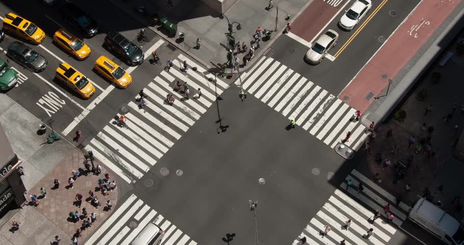 Bird's eye view of a busy intersection in Midtown Manhattan. Looking down on the streets of New York. Yellow taxis, city buses, cars, and people cross through the intersection going to work,timelapse. Royalty-Free Stock Footage #24098644