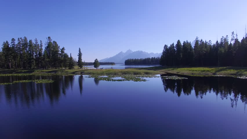 Camera flies over a calm Jackson Lake with mountains along the horizon