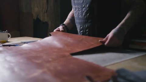 Craftsman work with big peace of leather at workshop, slow motion, close up