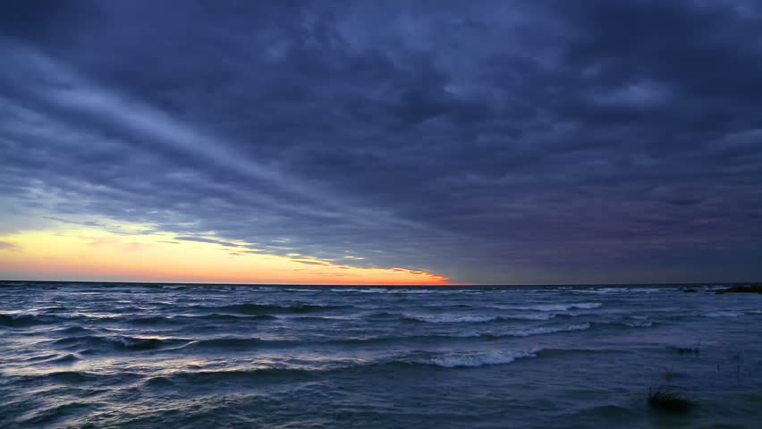 Looping video features a dramatic cloudy sky at sunset over Lake Michigan with rolling waves coming to shore. Shot at Manistique, Michigan.