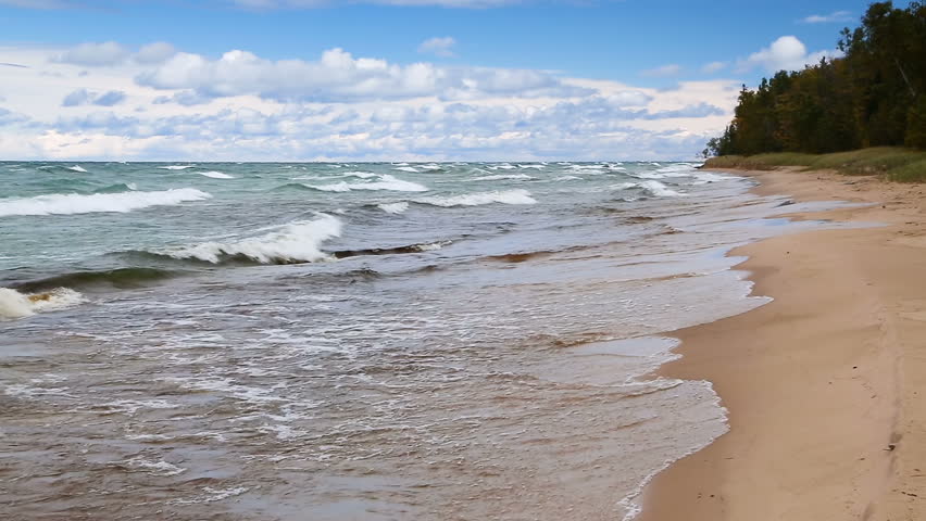 Waves break on the sandy Twelve Mile Beach at Pictured Rocks National Lakeshore in Upper Peninsula Michigan on a windy day with blue sky and white clouds. Looping.
