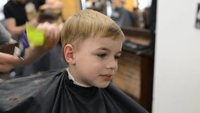 Haircutter male with client child in the barbers. Hairdresser using trimmer in barbershop. Happy cute kid sitting on the chair in hairdressing salon.