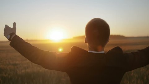 Slow motion of man in suit raising his hands up against the sun. Young man feeling a sense of accomplishment.