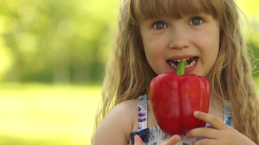 Close-up portrait of a happy girl holding a vegetable in the teeth
