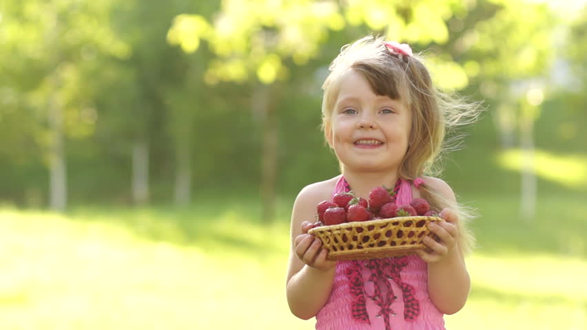 Child holding basket of strawberries and looking at camera

