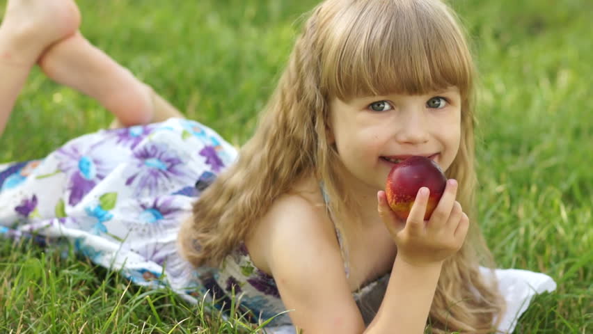 Girl lying on the grass and eating a peach
