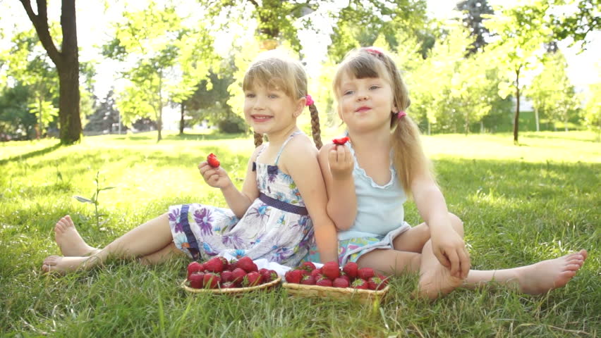Funny girls eating strawberries. Sitting on the grass
