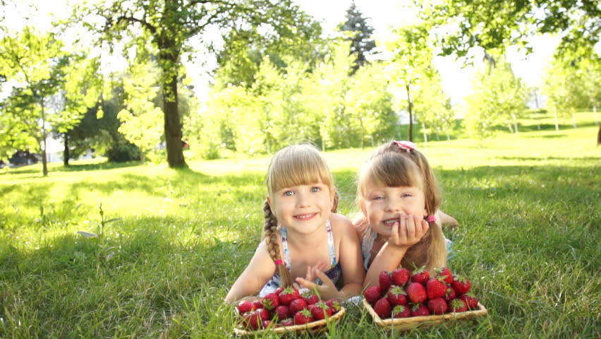 Laughing girls lying on the grass near strawberries
