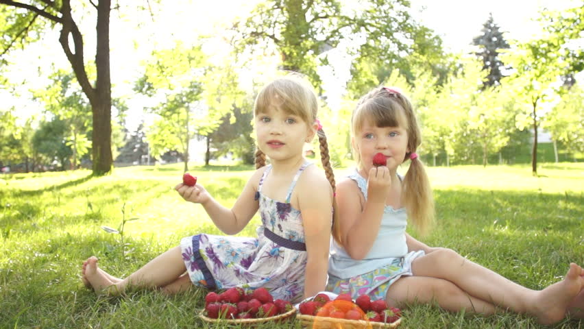 Happy kids eat strawberries. Sitting on the grass. Dolly HD
