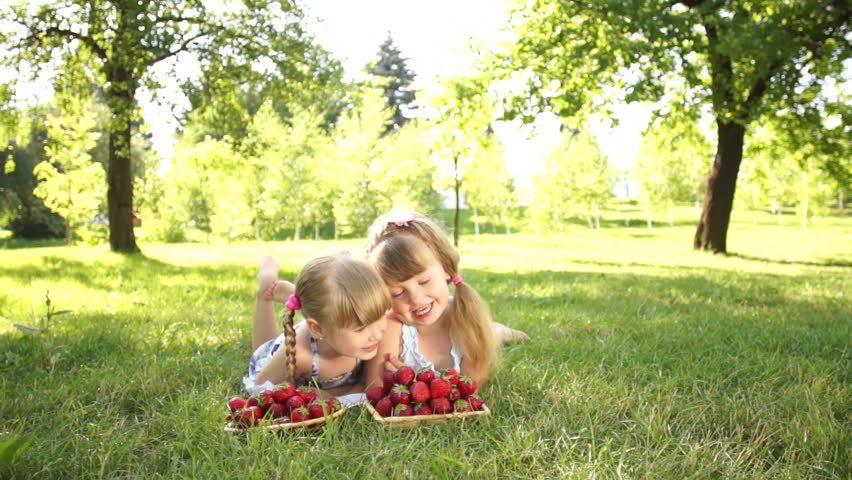 Laughing children lie on the grass. They eat strawberries

