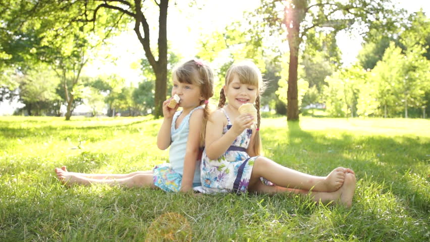 Girls eating ice cream. Sitting on the grass
