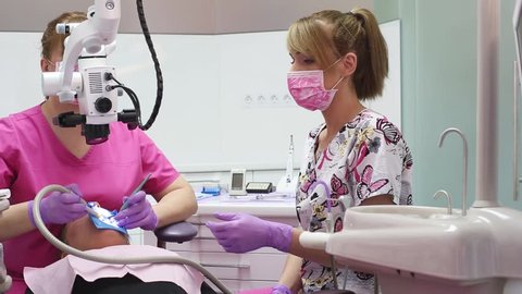 Health care in dental office. Female dentist treating a patient with dental microscope and medical assistant helping her.