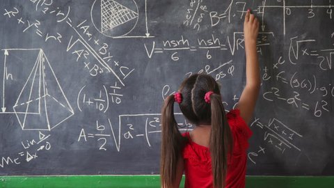 Concepts on blackboard at school. Young people, students and pupils in classroom. Smart hispanic girl writing math formula on board during lesson. Portrait of female child smiling, looking at camera
