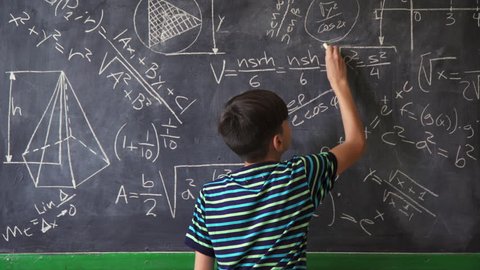 Concept on blackboard at school. Young people, student and pupil in classroom. Smart hispanic boy writing math formula on board during lesson. Portrait of male child smiling, looking at camera
