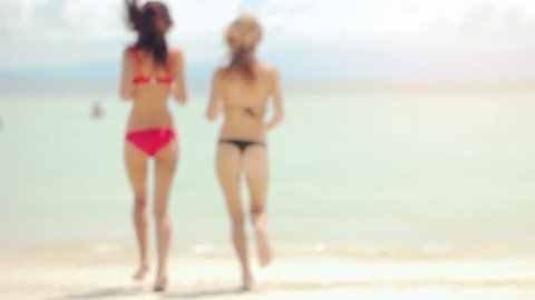 Rear view of two beautiful young women on the beach, run into sea, sexy butt